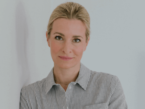 Eine Frau mit einem gestreiften Hemd steht vor einem neutralen Hintergrund und schaut freundlich in die Kamera.