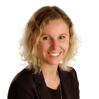 Porträt einer lächelnden Frau mit lockigem, schulterlangem Haar in einem dunklen Blazer, vor einem weißen Hintergrund.