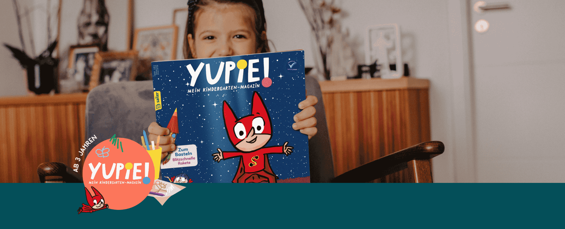Ein Kind hält eine Ausgabe des Magazins 'Yupie! Mein Kindergarten-Magazin', das von Sailer Verlag veröffentlicht wird. Auf dem Cover des Magazins ist eine Illustration eines fröhlichen Maskottchens in einem roten Kostüm vor einem dunkelblauen, sternenklaren Hintergrund abgebildet. Der Text auf dem Cover weist auf Aktivitäten wie Basteln hin. Unten auf dem Bild ist ein großes Logo des Magazins mit dem Hinweis 'Ab 3 Jahren'.