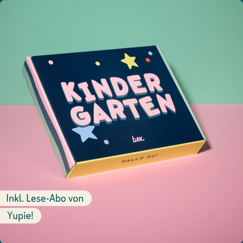 Eine bunt gestaltete Box mit der Aufschrift 'KINDERGARTEN' liegt auf einem zweifarbigen Hintergrund in Mintgrün und Rosa. Die Box ist dunkelblau mit bunten Stern- und Punktmotiven. Darunter der Text 'Hallo Du!' auf gelbem Rand. Links unten der Text 'Inkl. Lese-Abo von Yupie!'.